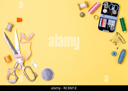Composition with threads and sewing accessories - scissors, centimeter, pins on yellow background. Stock Photo