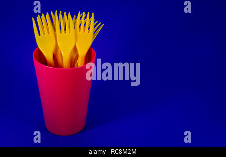 A pile of yellow plastic forks in a plastic pink mug on blue background Stock Photo
