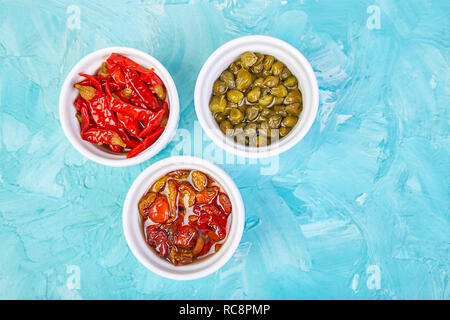 Italian preserved set - marinated capers and pepper, Sundried tomatoes in white bowls. Mediterranean. Copy space. Stock Photo