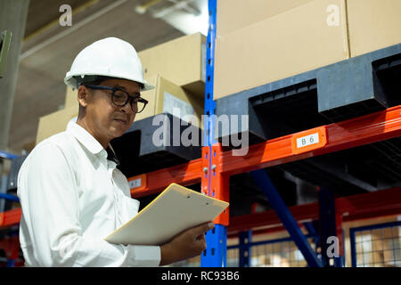 Warehouse manager asian checking his inventory in a large warehouse - Image Stock Photo