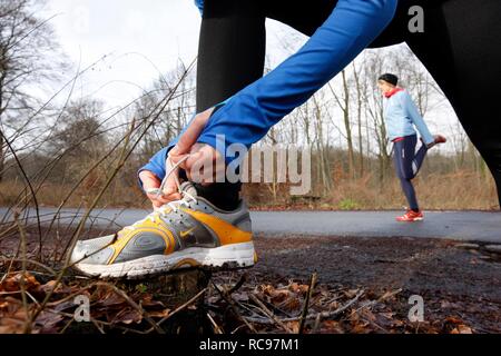 Two young women tying their shoes and stretching before jogging in winter, wearing wind and waterproof performance apparel Stock Photo
