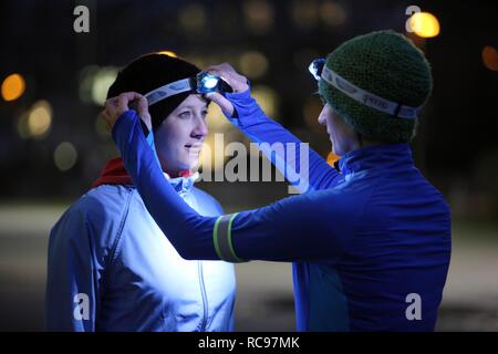 Two young women preparing to go jogging at dusk in winter, putting on reflector strips and LED headlamps, wearing reflective Stock Photo
