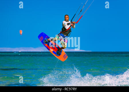 Egypt, Hurghada - 30 November, 2017: The kitesurfer soaring in the blue sky over the Red sea surface. Amazing wave splash. The extreme water sport activity. Popular tourist attraction. Stock Photo