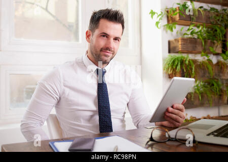 Businessman wearing shirt and tie and using digital tablet while sitting at office desk and working on new project. Stock Photo