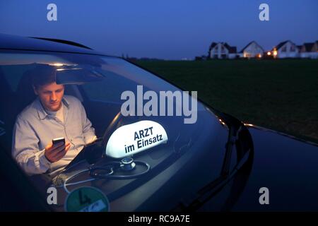 Young GP, general practitioner working in the country, making phone call in his car after an evening home visit, car displaying Stock Photo