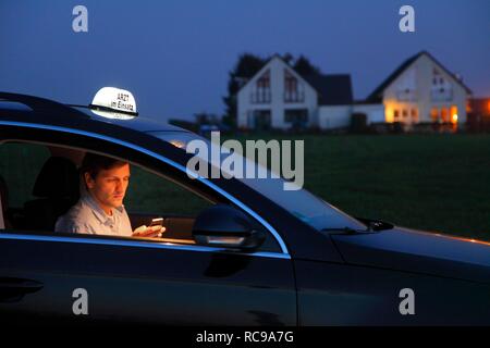 Young GP, general practitioner working in the country, making phone call in his car after an evening home visit, car displaying Stock Photo