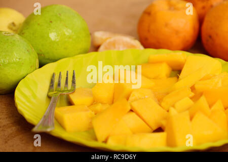 Beautifully sliced pieces of papaya on a  plate with a fork around guava and orange fruit Stock Photo