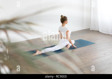 Sporty young woman doing yoga practice on white background at home. Stock Photo