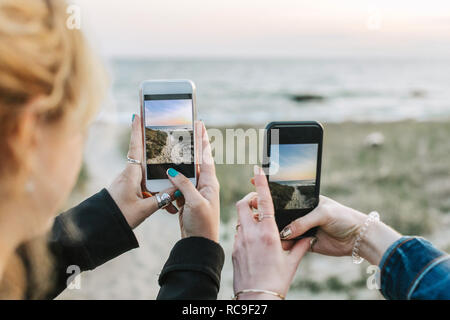 Two young women photographing beach on smartphones, over shoulder view, Menemsha, Martha's Vineyard, Massachusetts, USA Stock Photo