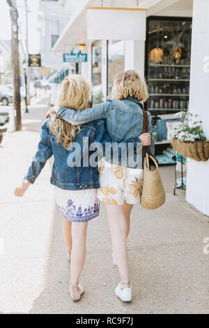Two young female friends strolling along village sidewalk, rear view, Menemsha, Martha's Vineyard, Massachusetts, USA Stock Photo