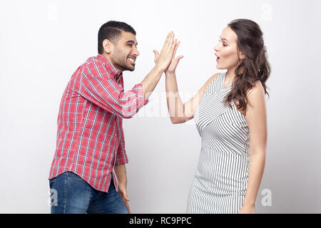 high five. Profile side view portrait of happy handsome man in red checkered shirt and beautiful woman in white striped dress standing and celebraitin Stock Photo