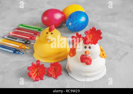 Multi-colored Easter eggs lie next to paint for coloring and marzipan Easter cakes in the shape of chickens. Stock Photo