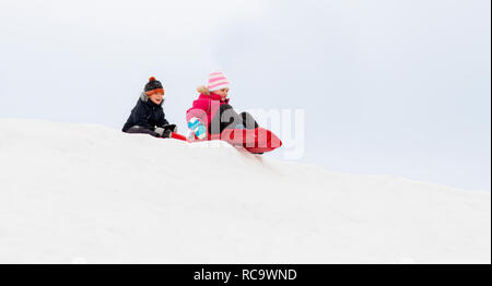 happy kids sliding on sleds down hill in winter Stock Photo
