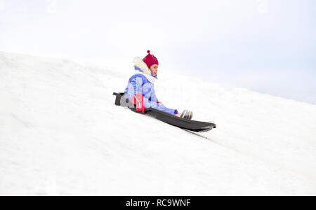 happy little girl sliding down on sled in winter Stock Photo