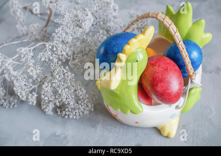 Multi-colored Easter eggs lie on a white plate in the shape of a chicken next to paint for coloring and Easter cakes. Copy space. Stock Photo