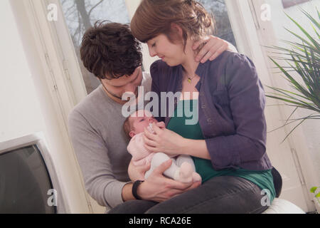 Junge Eltern halten ihre neugeborene Tochter im Arm, das Kind ist 12 Tage alt | young parents holding her new born baby in her arms - the baby ist 12  Stock Photo
