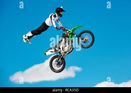 Racer on motorcycle participates in motocross cross-country in flight, jumps and takes off on springboard against sky. Concept active extreme rest. Stock Photo