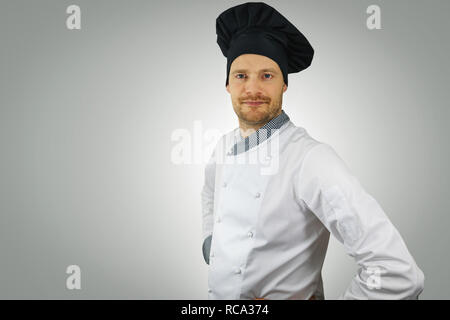 young chef in uniform with hands on hips standing on gray background Stock Photo