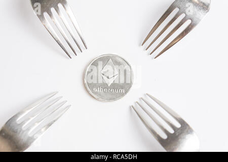 Ethereum cryptocurreny silver coin placed between forks on white background, hard fork Stock Photo