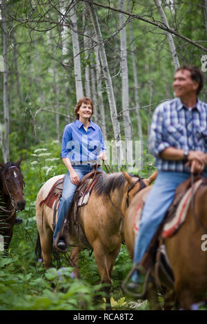 Mature couple riding horses through forest Stock Photo