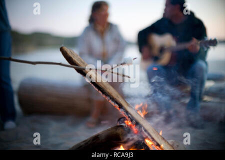 Marshmallow on a stick is roasted over a camp fire on a beach. Stock Photo