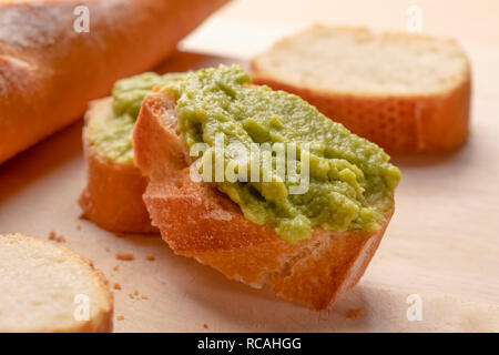 Crispy appetizing sandwiches from fresh baguette with a cream useful avacado cream on a chopped board. With scattered crumbs Stock Photo
