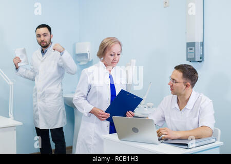 Beautiful mature serious doctors are using a laptop, discussing diagnosis while standing in clinic Stock Photo