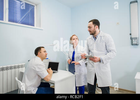 Medical staff discussing over medical reports using laptop and tablet pc. Healthcare professionals having discussion in hospital office. Stock Photo