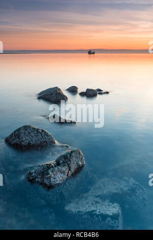 Calm peaceful sunset on Holy Island, lovely warm pastel colours in the sky & cool blues in the sea, the rocks standing proudly above & below the sea Stock Photo