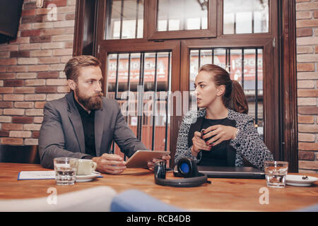 Businesspeople discussing while using digital tablet and drinking coffee while working in cafe Stock Photo