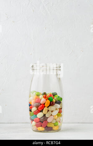 Glass jar full of colorful jelly beans on rustic wooden table over grey background Stock Photo