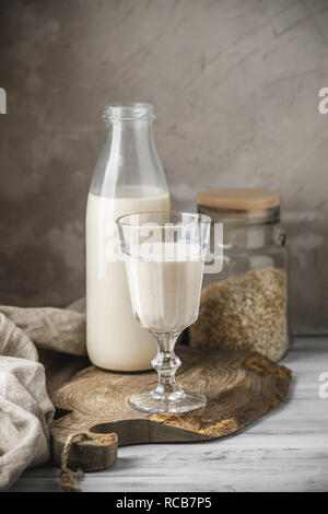 Non dairy oat milk for vegan diet. Oat flakes in glass jar and glass bottle of milk on rustic background Stock Photo