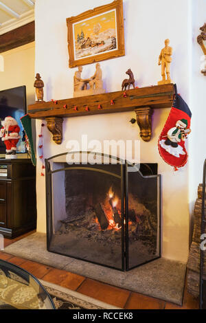 Lit wood burning fireplace decorated with Christmas stockings inside an old circa 1886 Canadiana cottage style home Stock Photo
