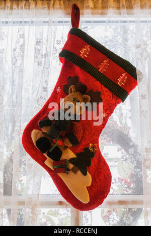Red Christmas stocking decorated with brown teddy bear hung on a window inside an old home Stock Photo