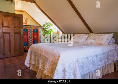 Master bedroom with large pinewood floorboards, queen size bed and colourful wooden antique armoire with diamond point design in old 1835 house Stock Photo