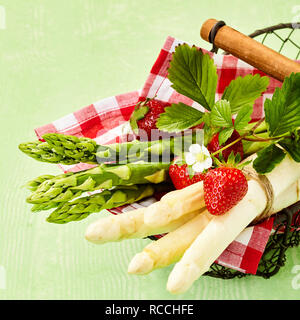 Basket with fresh green and white asparagus bunches decorated with ripe strawberry. Viewed from above in close-up Stock Photo
