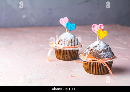 Tasty delicious homemade muffin on light pink living coral stone concrete surface with knitting hearts, copy space. Sweet food for valentines day. Stock Photo