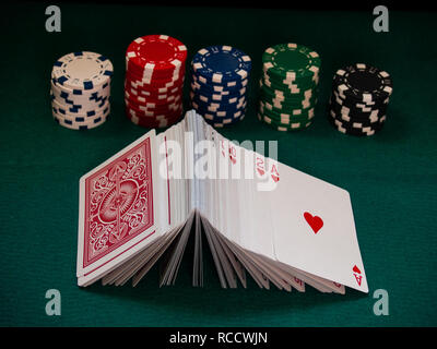A deck of poker cards and poker chips of various colors on a green mat Stock Photo
