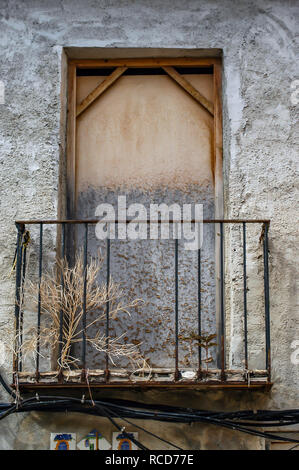Looking up at security boarded up old window space with tatty Juliet balcony in old village house Stock Photo
