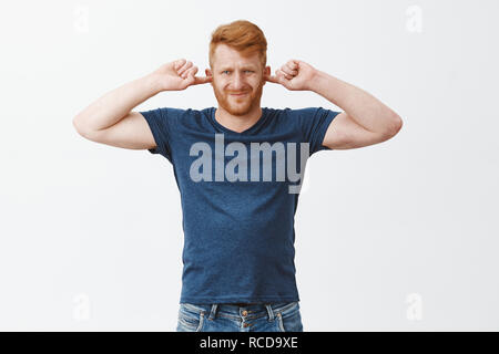 Boyfriend hates girlfriend music taste. Portrait of displeased attractive strong european man with ginger hair, covering ears, frowning and pursing lips from discomfort, being annoyed with loud sound Stock Photo