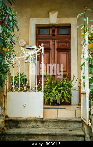 Looking up steps at house large double wooden doors with two small windows above door and gated patio with green plants Stock Photo