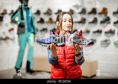 Young woman choosing trail shoes for mountain hiking in the modern sports shop Stock Photo