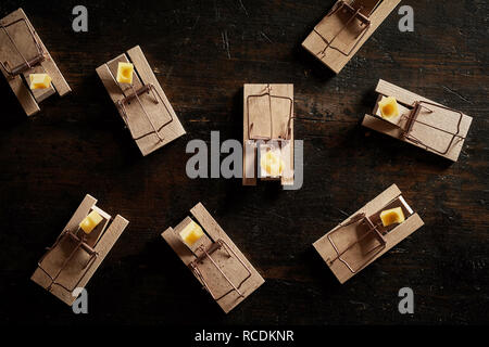 Many cocked spring wooden bar mouse traps loaded with cheese, viewed from above on dark wooden surface background Stock Photo