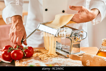 Italian chef making homemade spaghetti pasta using a cutting machine holding the rolled dough in his hand in a close up view Stock Photo