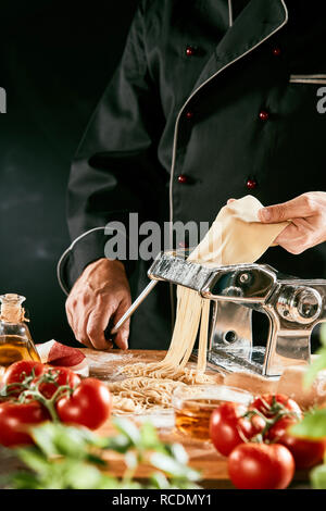 Italian chef preparing homemade pasta noodles using a manual cutter standing turning the handle as he guides the dough Stock Photo
