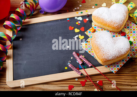 Easter treats and decorations with copy space on blackboard in wooden frame on the table with heart-shaped cookies, confetti and firecrackers, viewed  Stock Photo