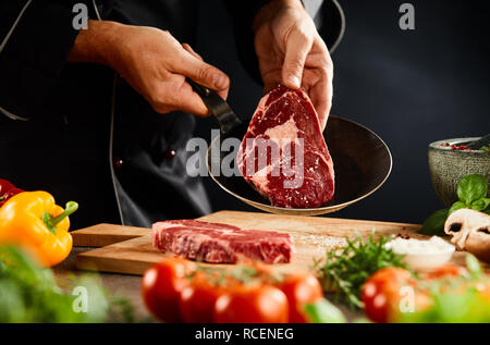 Chef placing a raw steak into a skillet for braising or grilling with fresh vegetables in the foreground