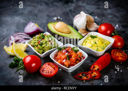 Selection of mexican sauces - salsa, guacamole, cheese sauce and ingredients, dark stone background Stock Photo