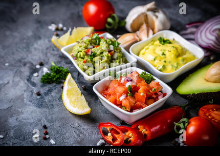 Selection of mexican sauces - salsa, guacamole, cheese sauce and ingredients, dark stone background Stock Photo