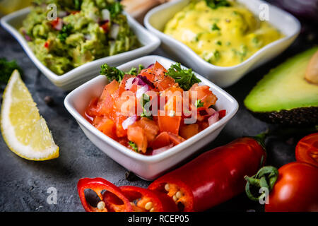 Selection of mexican sauces - salsa, guacamole, cheese sauce and ingredients, dark stone background Stock Photo